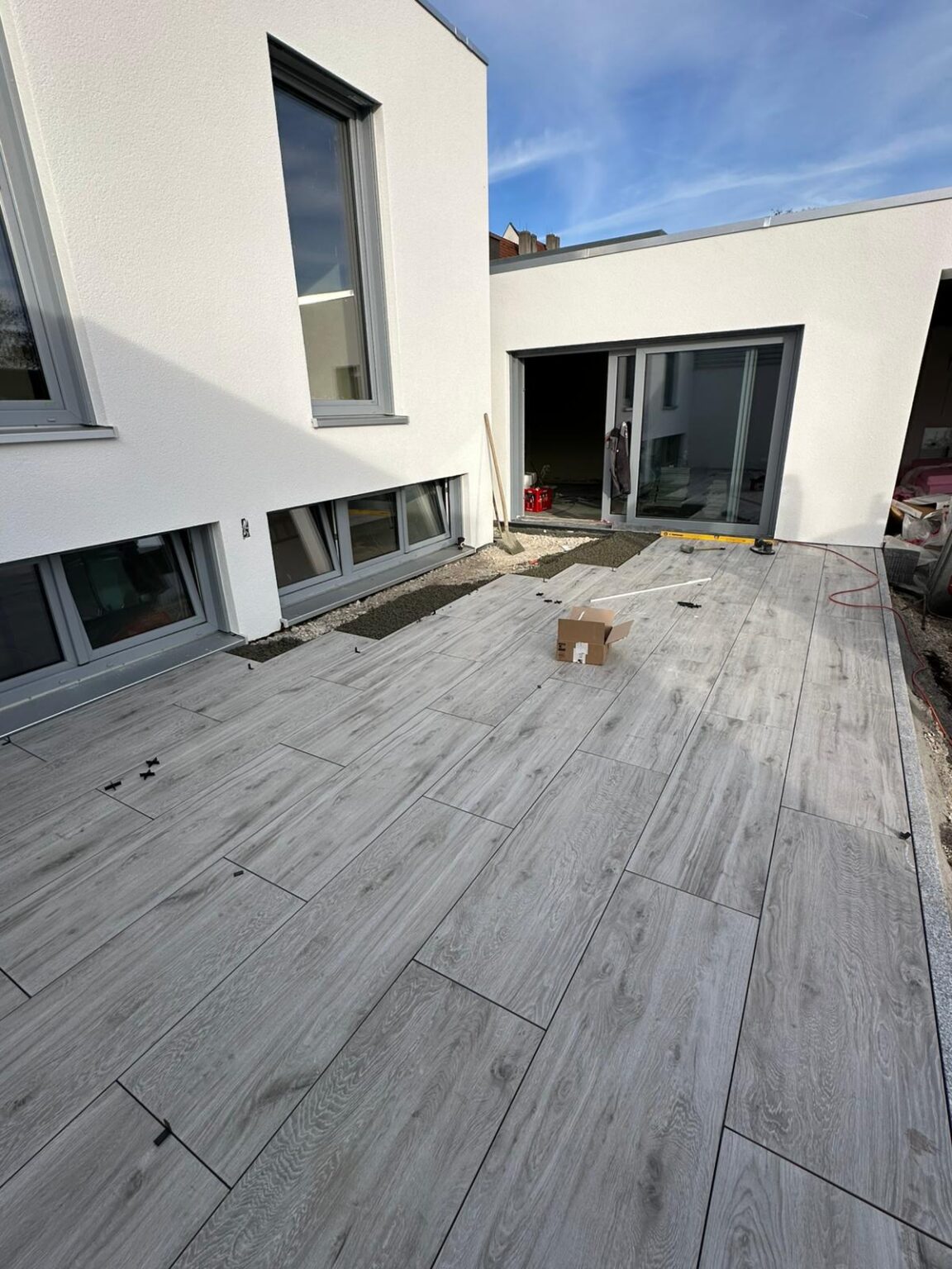 Graue Holz-Optik Fliesen auf einer frisch verlegten Terrasse eines Bungalows.
